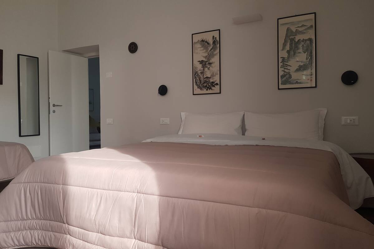 Een slaapkamer met een groot bed, twee wandklokken en twee ingelijste schilderijen.