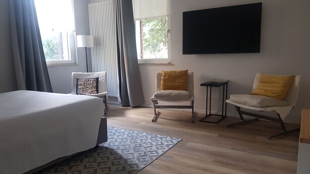 Une chambre d’hôtel avec un lit, deux chaises, une télévision et une fenêtre avec des rideaux.