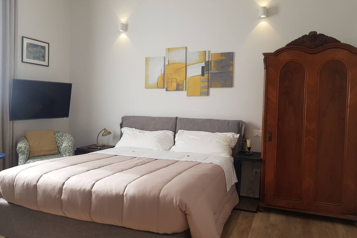 Een slaapkamer met een bed, nachtkastjes, een kledingkast, een flatscreen-tv en abstracte wanddecoratie.