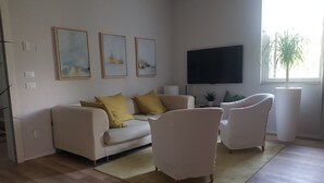 Un salon moderne comprenant un canapé, deux fauteuils, un téléviseur à écran plat et trois œuvres d’art encadrées accrochées au mur.