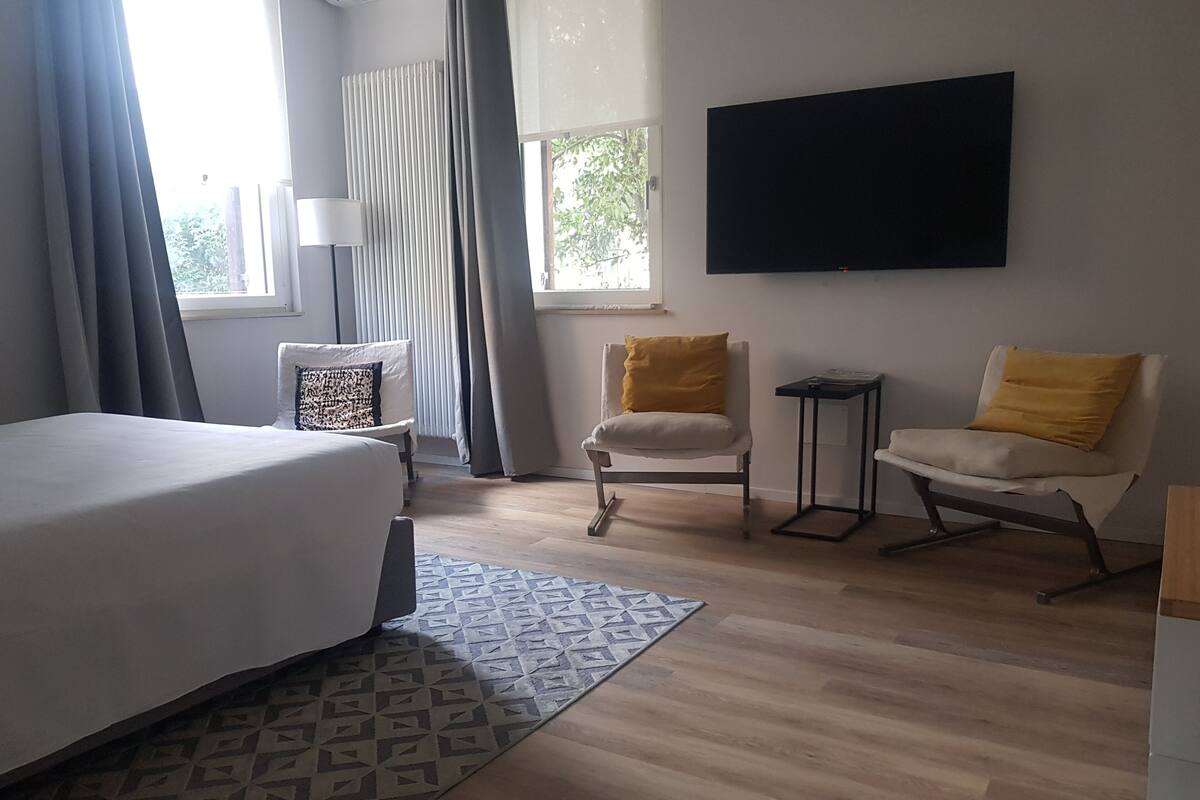 Een slaapkamer met een bed, twee stoelen, een televisie en een raam met gordijnen.