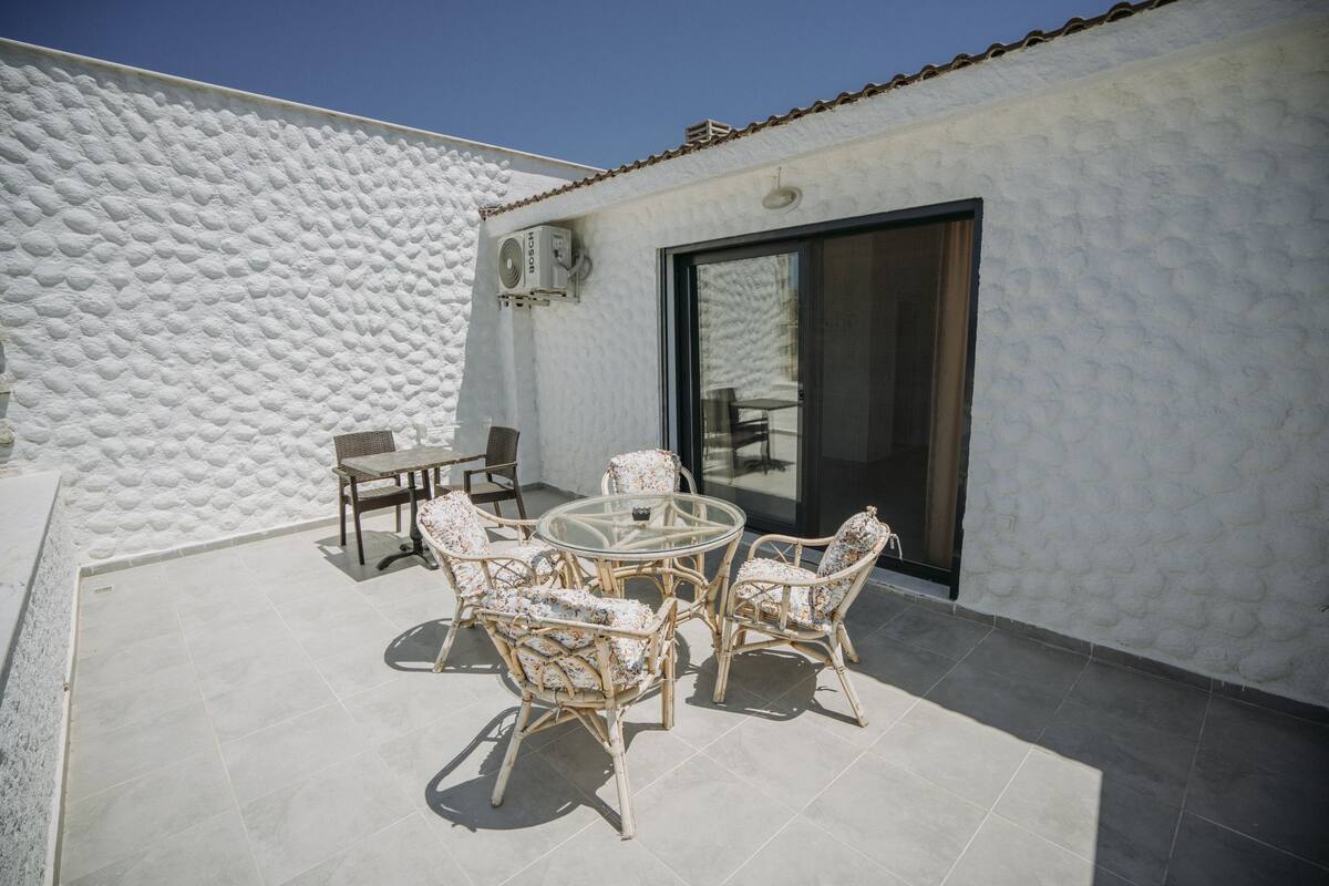 A patio with wicker furniture and a glass table, a white textured wall, and a sliding glass door.