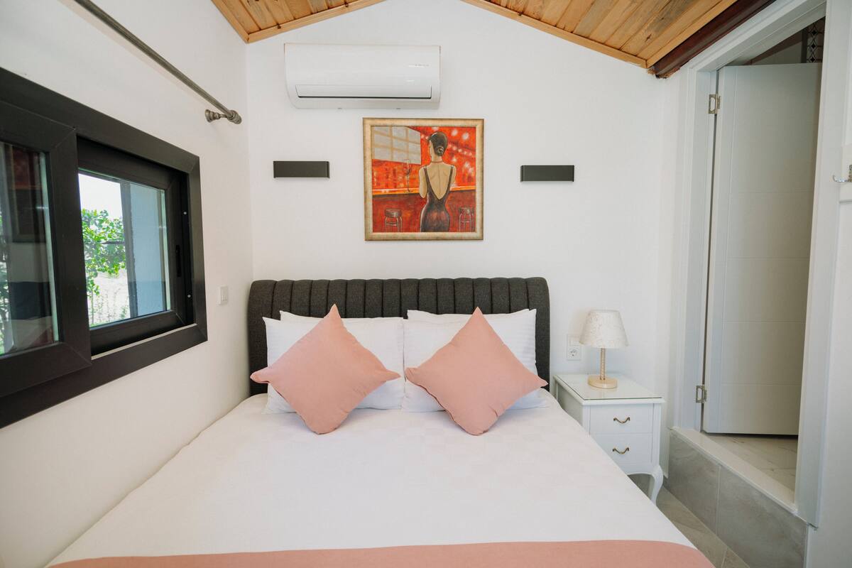 A bedroom with a bed, a nightstand, a lamp, and a painting on the wall.