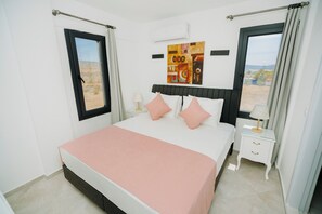 A bedroom with a bed, a nightstand, a window, and a painting on the wall.