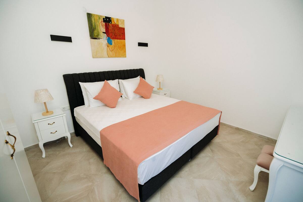A neatly arranged bedroom with a bed, bedside tables, and a wall-mounted artwork.