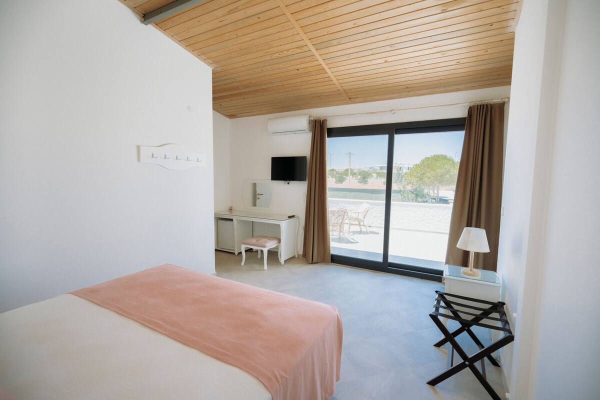 A bedroom with a bed, a desk, a chair, a TV, and a view of the outdoors.