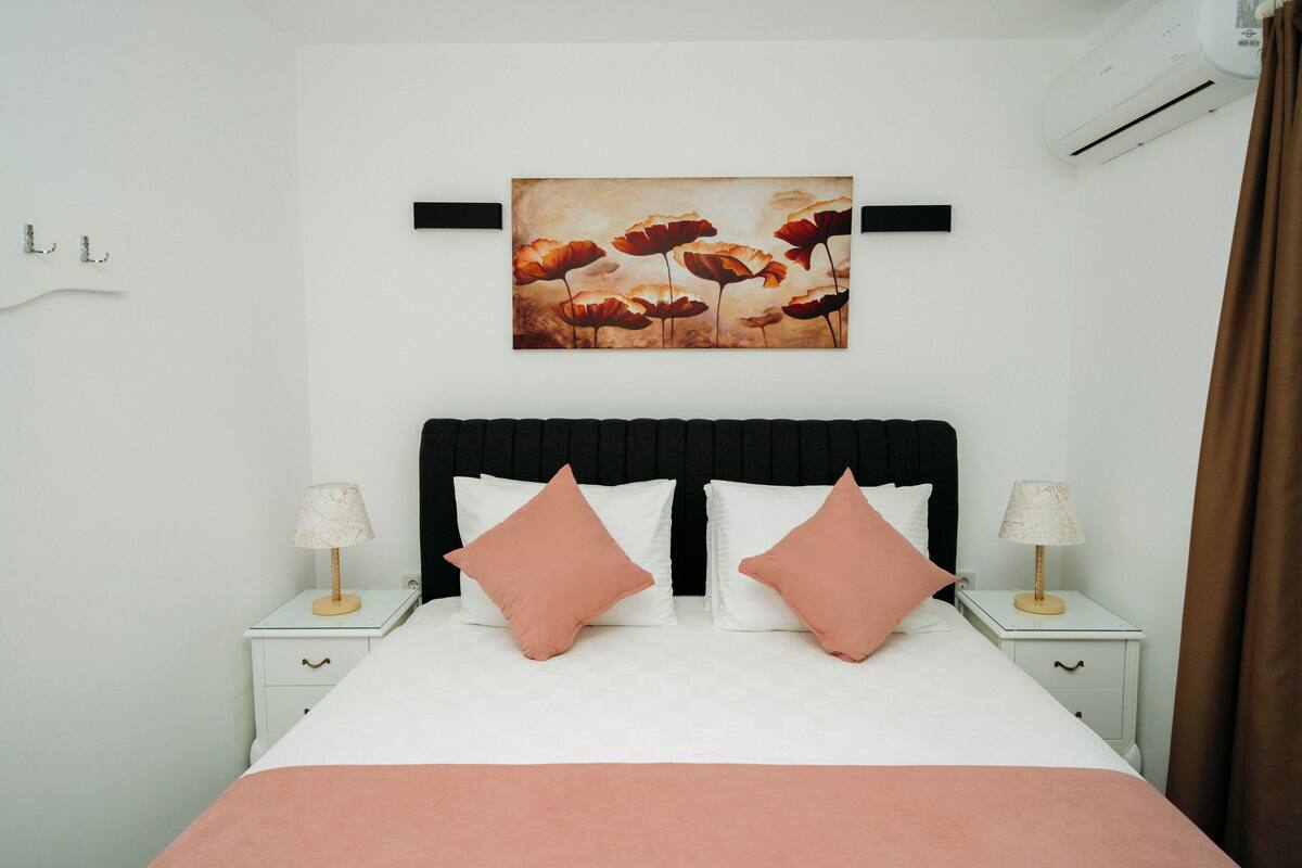 A neatly made bed with a black headboard, two bedside tables with lamps, and a wall-mounted artwork above the bed.
