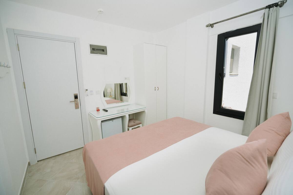 A bedroom with a bed, a desk, a chair, a wardrobe, and a window.