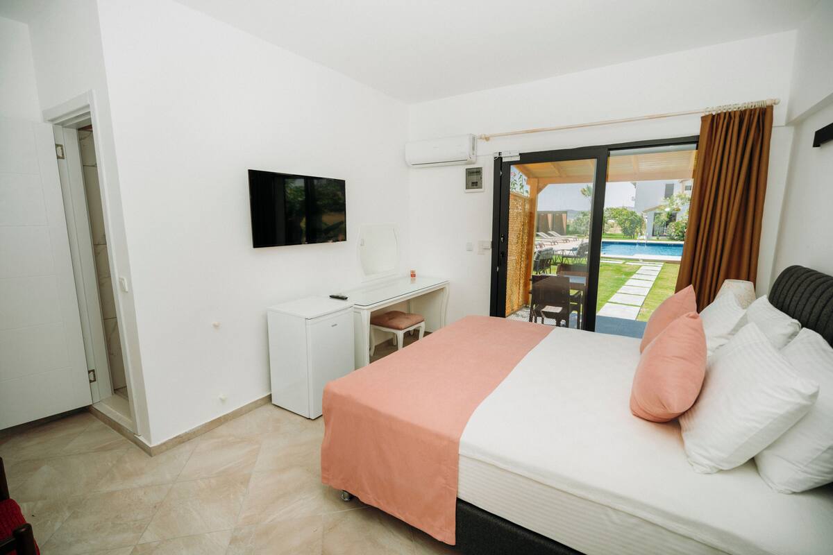A hotel room with a bed, a desk, a television, and a view of a swimming pool.