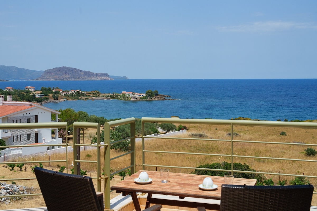 A balcony with a table and chairs overlooking a coastal view.