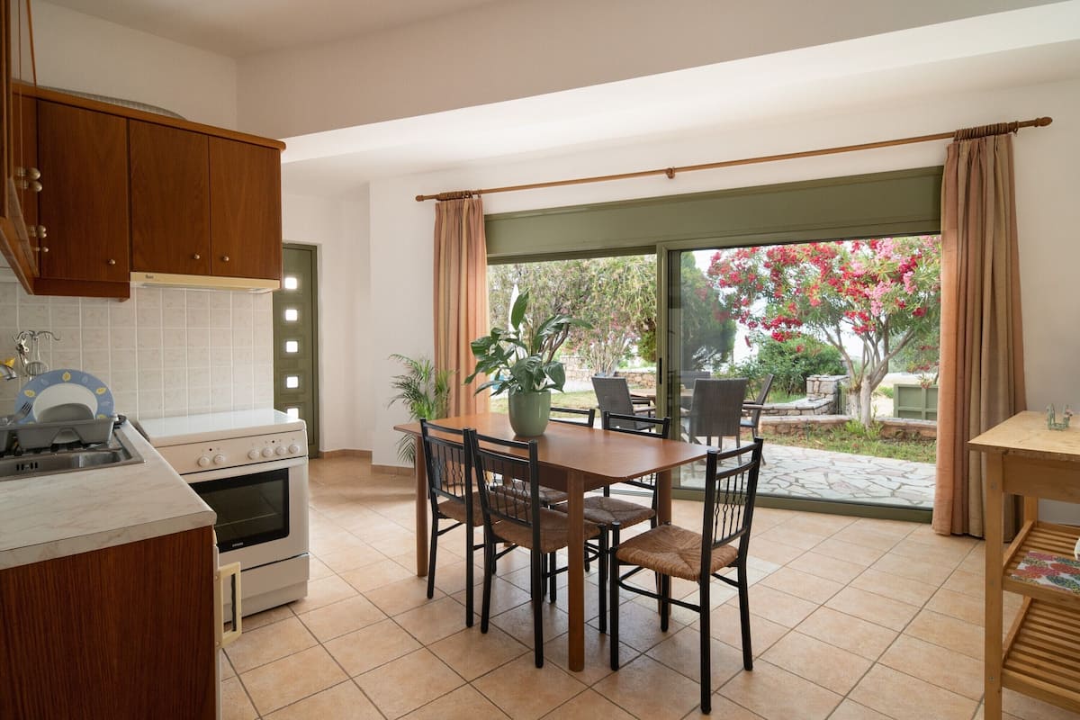 A kitchen with a dining area, a stove, and a large window with curtains.