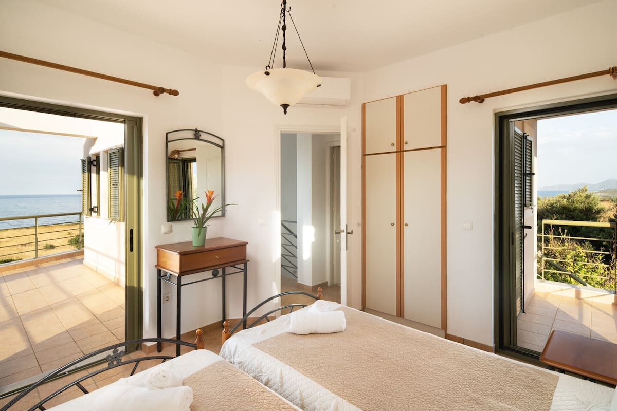 A bedroom with two beds, a bedside table, a mirror, and a view of the sea.