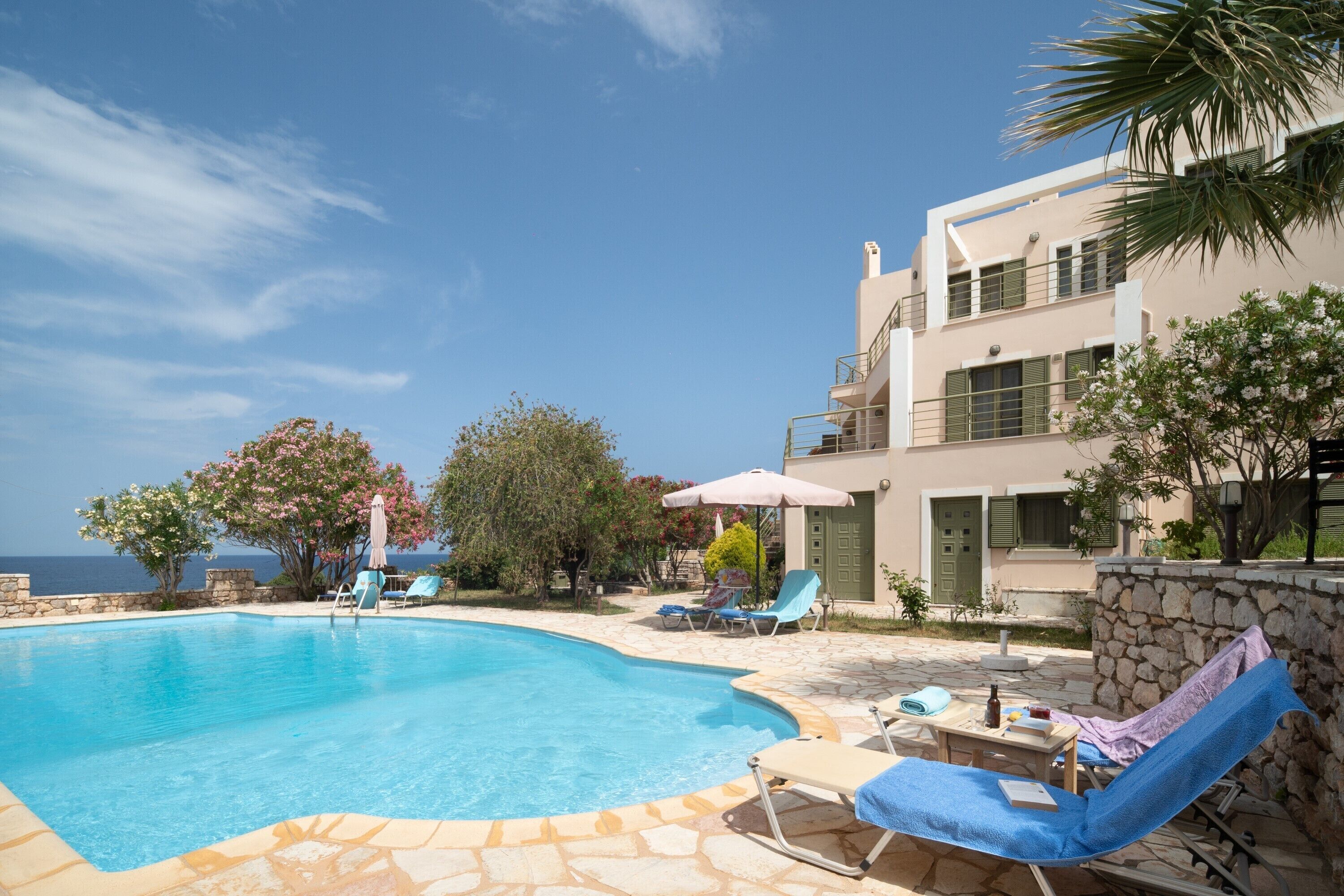 A swimming pool with lounge chairs and umbrellas, a stone wall, and a view of the sea.