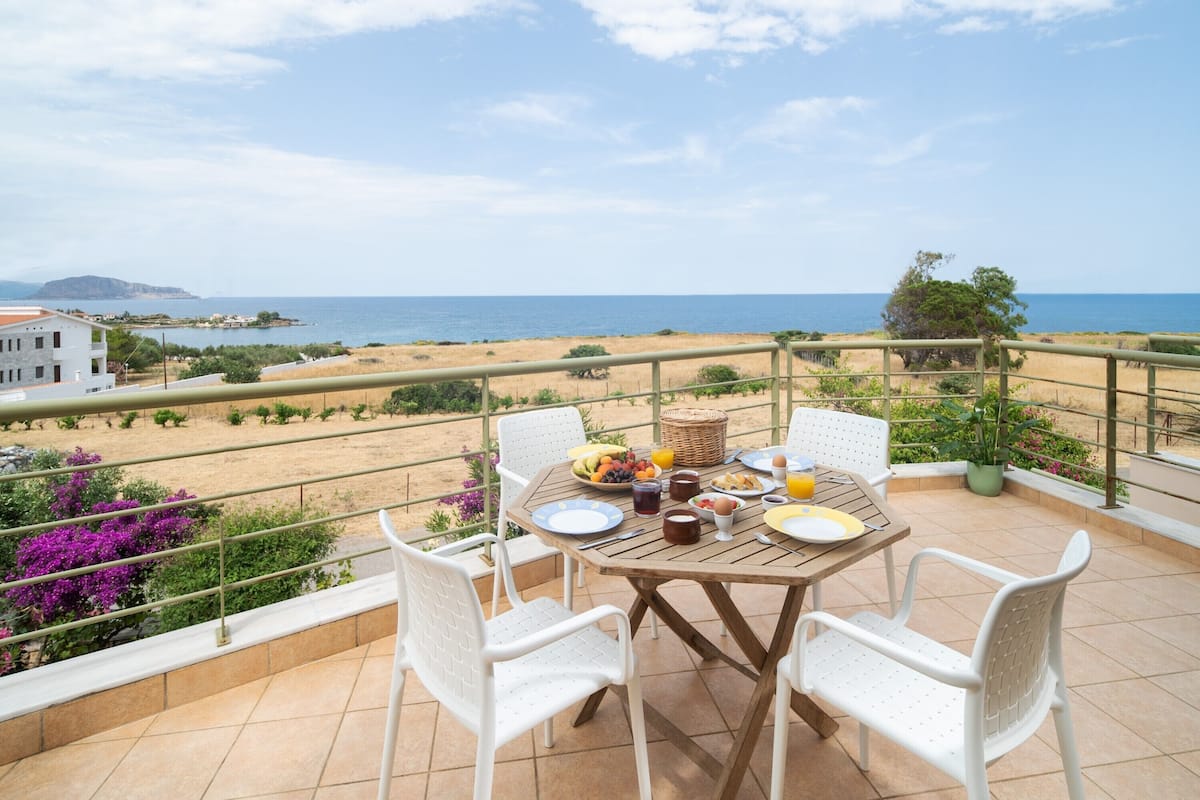 A terrace with a table set for breakfast, overlooking a beach and ocean.