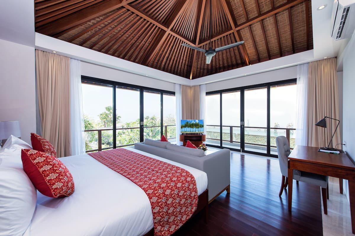 A hotel room with a large bed, a desk, and a balcony with a view of palm trees.
