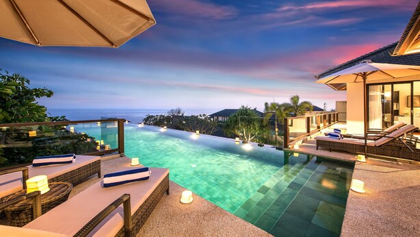 A poolside area with lounge chairs, a pergola, and a view of the ocean at sunset. - Karang Saujana Estate (Kutuh)