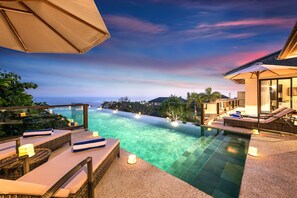 A poolside area with lounge chairs, a pergola, and a view of the ocean at sunset.
