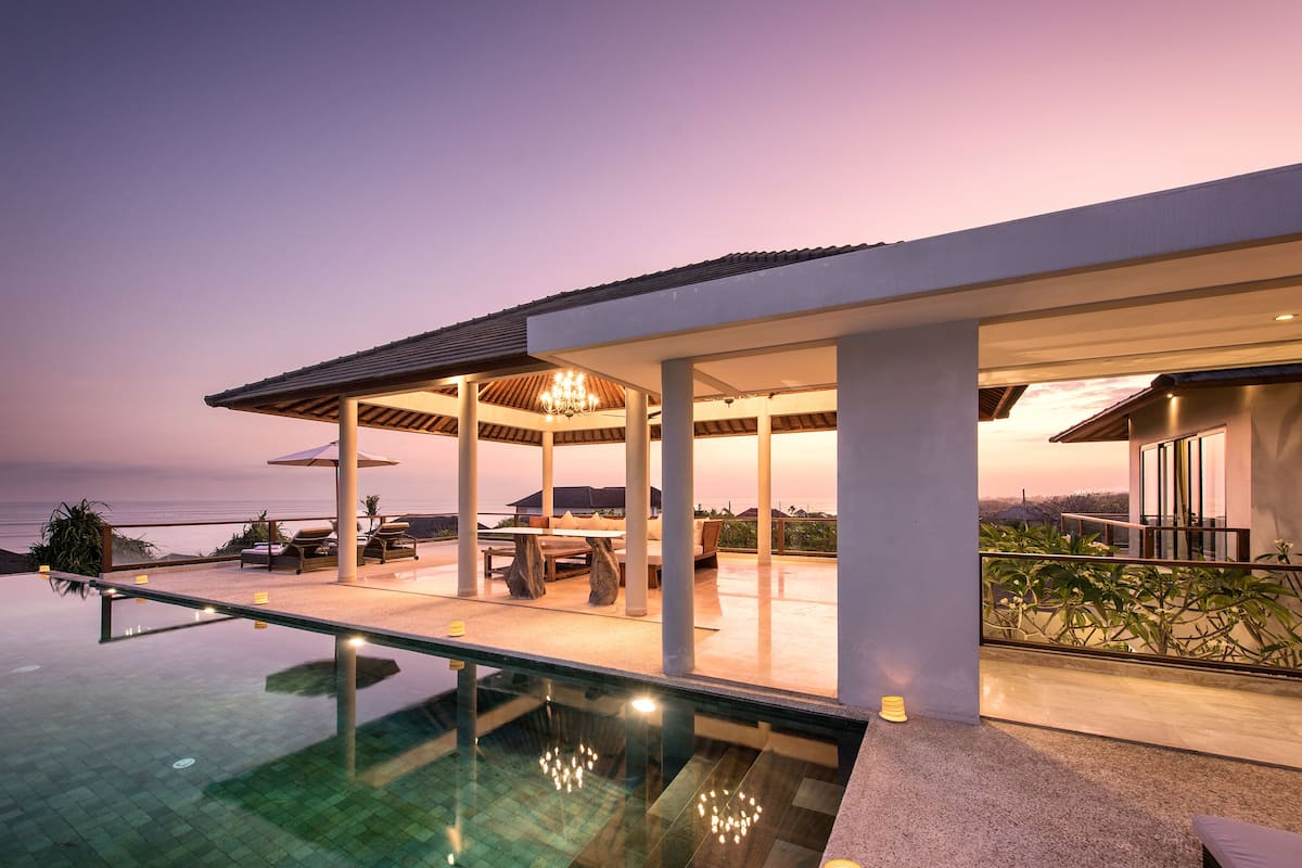 A modern outdoor pool area with a glass barrier, lounge chairs, and a dining table under a pergola.