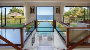A modern interior with a glass bridge leading to a balcony overlooking the ocean. - Karang Saujana Estate (Kutuh)