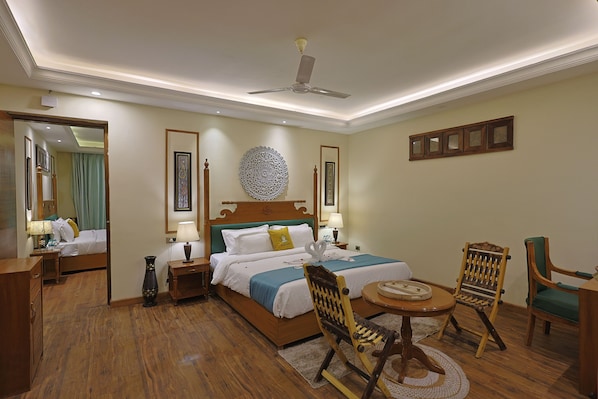 A hotel room with a bed, two chairs, a table, a ceiling fan, and a decorative wall piece. - Punarnava Resort & Spa (Dehradun)