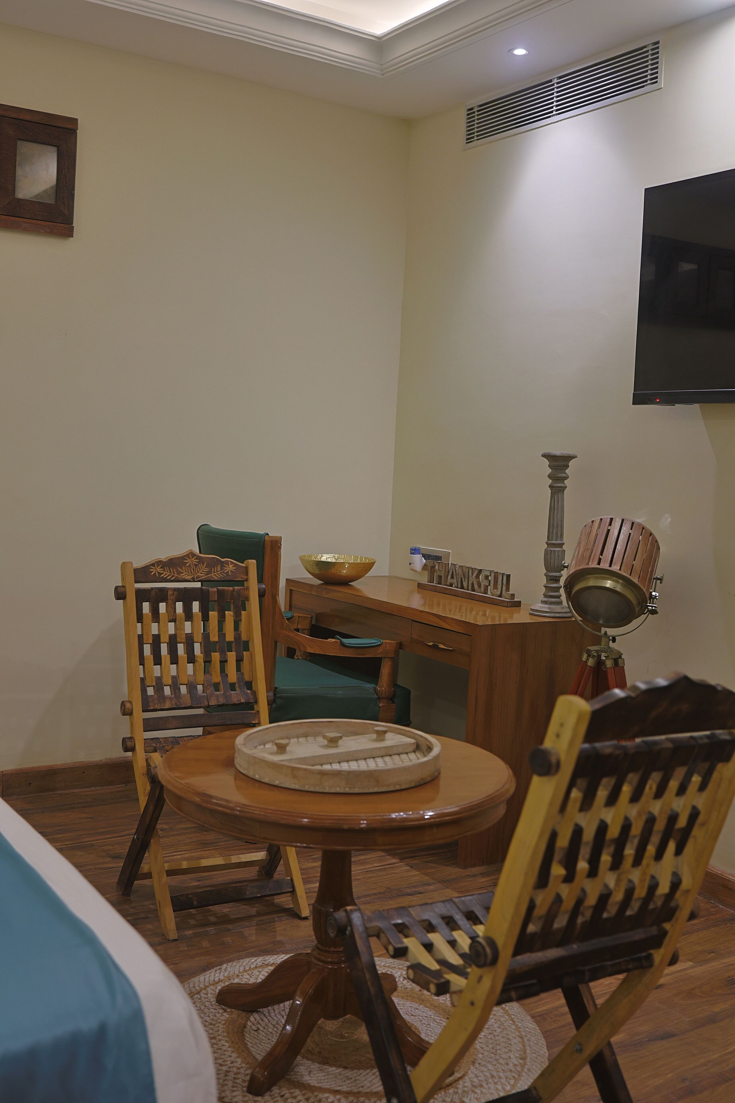 Una habitación pequeña con una mesa de madera, dos sillas, un mueble de madera y un televisor montado en la pared.