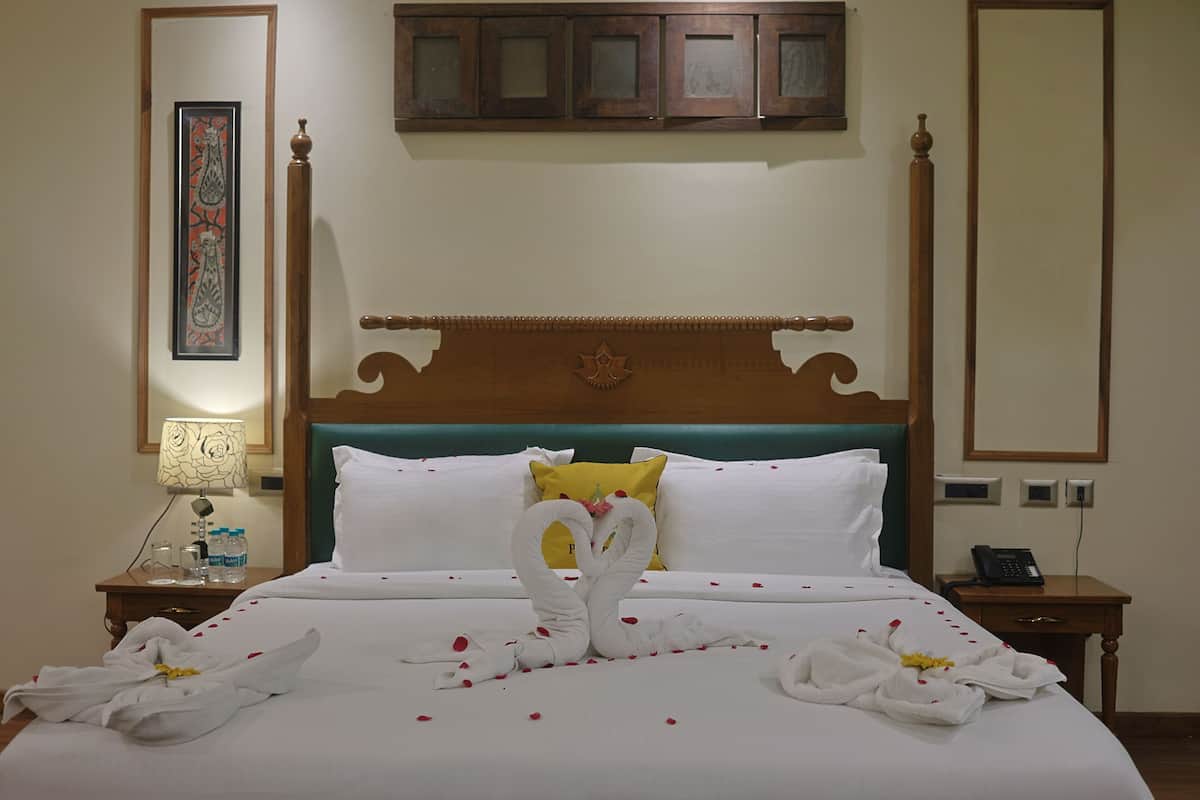 Quarto de hotel com uma cama grande, cabeceira de madeira, mesa de cabeceira com abajur e telefone fixado na parede.