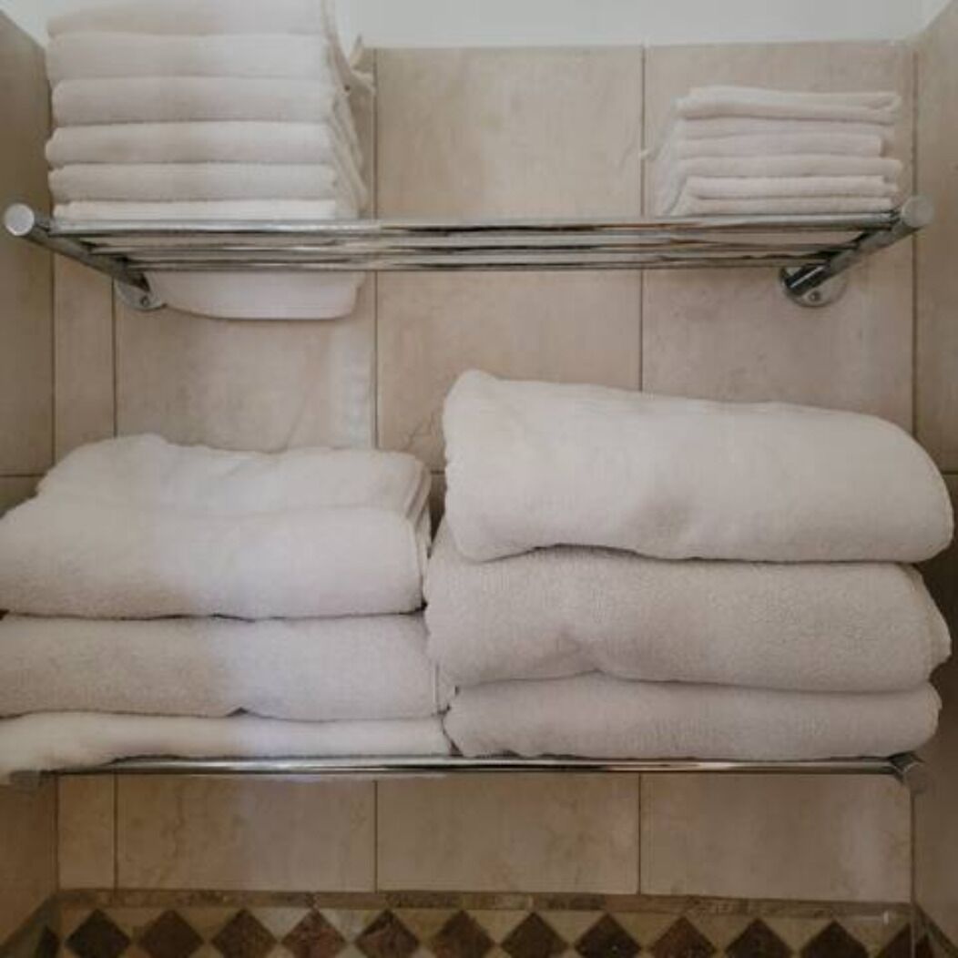 A bathroom with a tiled floor and a shelf holding neatly folded white towels.