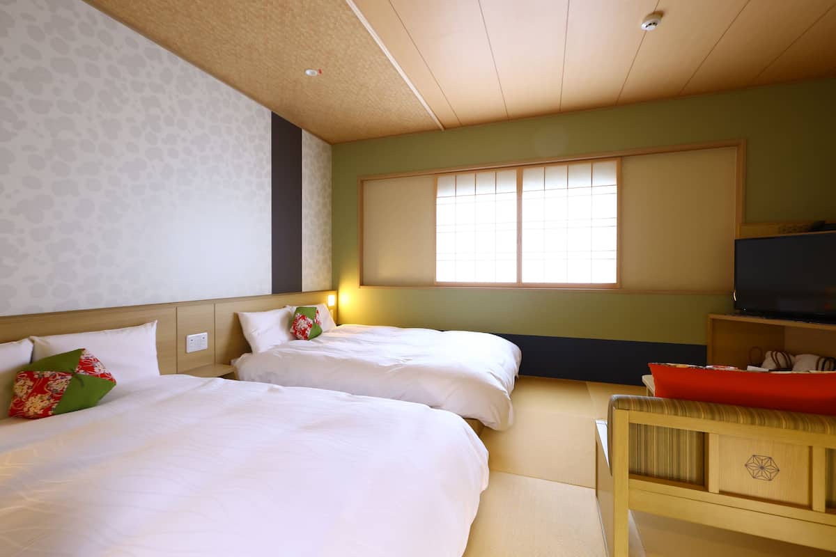 Ein Hotelzimmer mit zwei Betten, einem Fernseher und einem Fenster mit Jalousien.