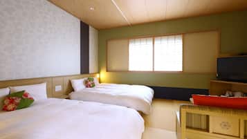A hotel room with two beds, a television, and a window with blinds.