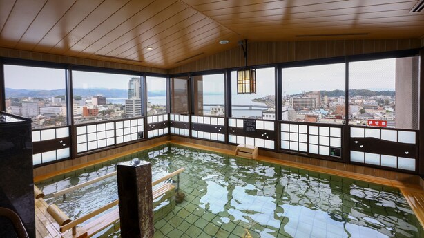 Un onsen japonais traditionnel, avec un plancher en bois et des tatamis, de grandes fenêtres offrant une vue sur la ville et un plafond en bois.