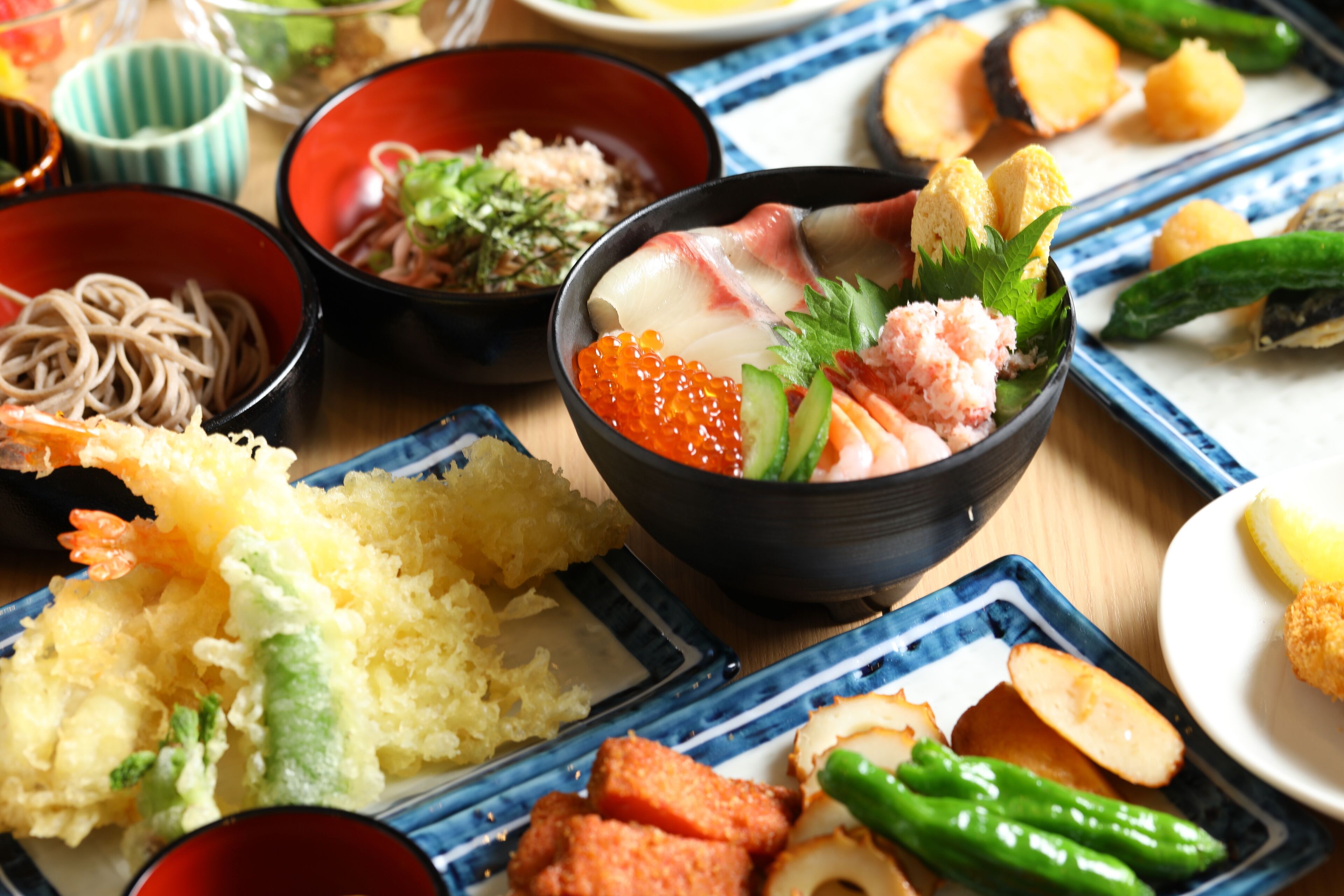 A variety of Japanese dishes including sushi, sashimi, and tempura on a wooden table.