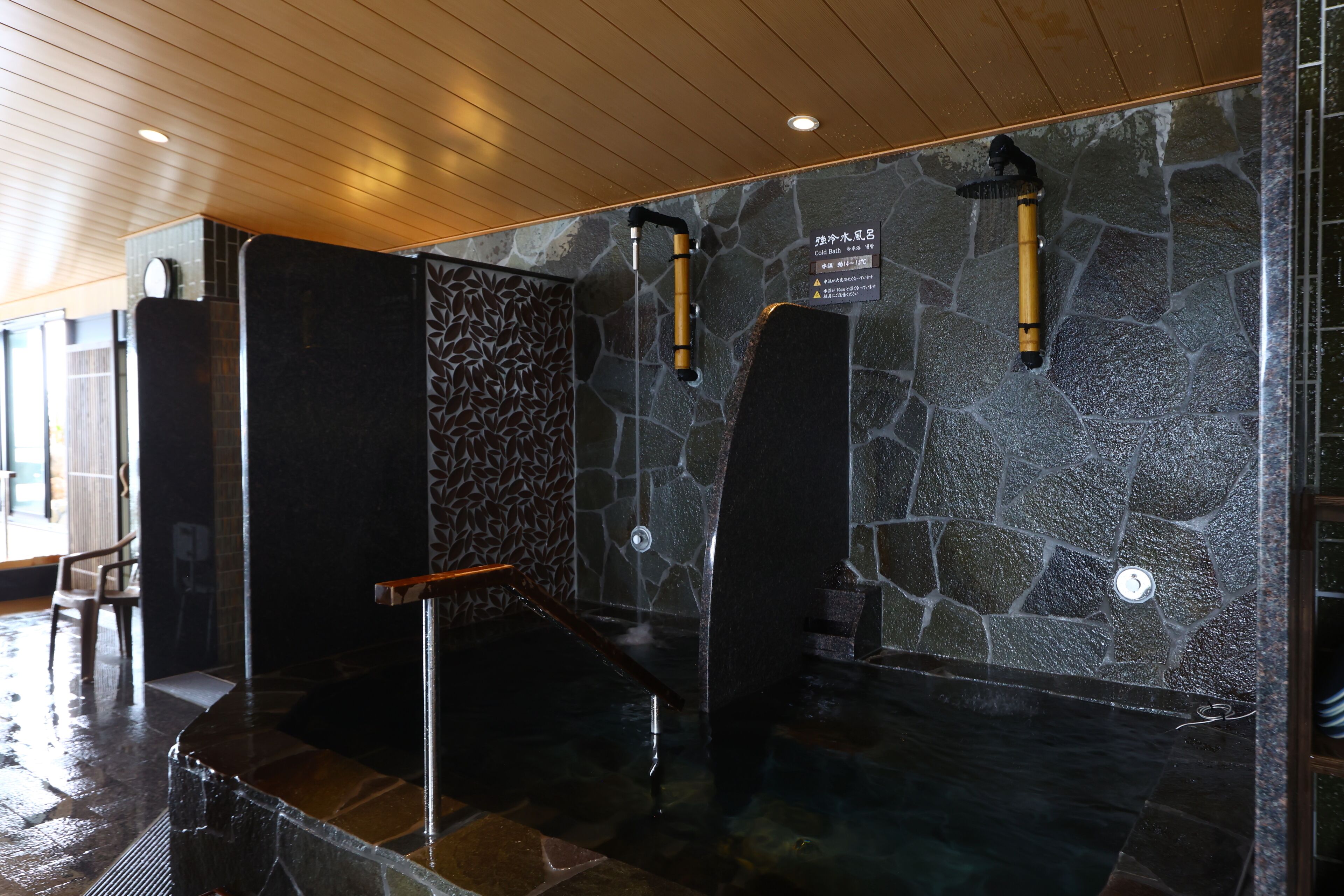A stone-walled sauna with a wooden ceiling, a bench, and a bench with a towel rack.