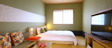 Una habitación con una cama, un sofá con cojines florales, una mesita y un televisor sobre un mueble de madera.