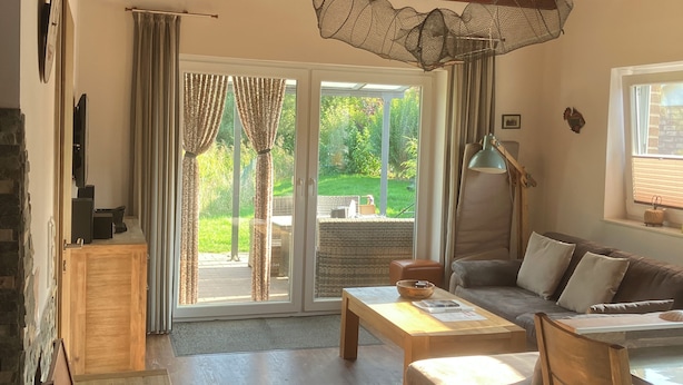 A cozy living room with a wooden ceiling, a sofa, a coffee table, and a dining area. - 500m zum Hundestrand, Eingezäunter Garten, Ebenerdig (Wurster Nordseeküste)