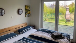 A bedroom with a wooden headboard, a bed with blue and white striped bedding, and a view of a green garden through a sliding glass door. - 500m zum Hundestrand, Eingezäunter Garten, Ebenerdig (Wurster Nordseeküste)