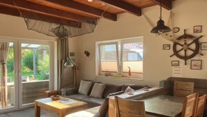 A cozy living area with a wooden ceiling, a sofa, a coffee table, and a dining table with chairs. - 500m zum Hundestrand, Eingezäunter Garten, Ebenerdig (Wurster Nordseeküste)