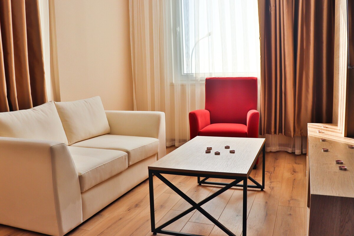 A modern living room with a beige sofa, a red armchair, a coffee table, and a foosball table.