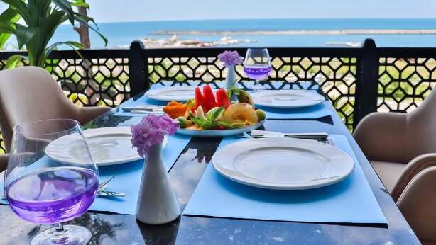 A table set for two with a view of the sea, a vase with purple flowers, and a plate of fruit. - The Sign Degirmen Hotel & Spa (Sile)