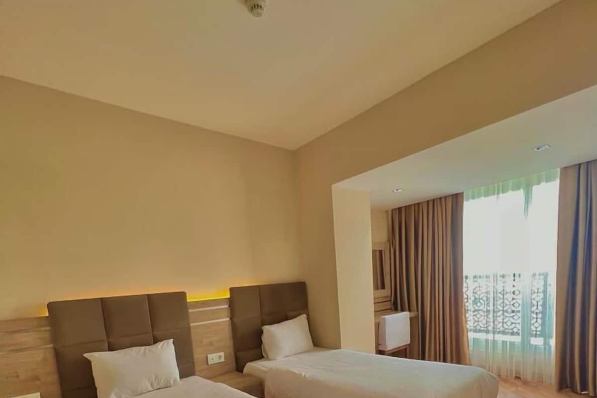 Habitació d'hotel amb dos llits, sòl de fusta i una finestra gran amb cortines.
