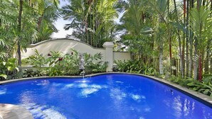 A swimming pool surrounded by lush tropical vegetation and a white wall with a decorative arch. - MUNBILLA 6 @ PALM COVE (PALM COVE)