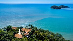 An aerial view of a coastal area with a cluster of houses surrounded by dense greenery, overlooking a calm sea with two small islands in the distance. - MUNBILLA 6 @ PALM COVE (PALM COVE)