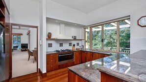 A modern kitchen with wooden cabinets, a granite countertop, and a large window overlooking a deck. - MUNBILLA 6 @ PALM COVE (PALM COVE)