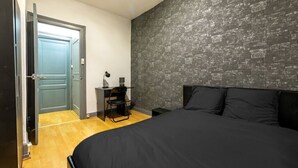 Een slaapkamer met een groot bed, een bureau met stoel, een deur en een structuurwand.
