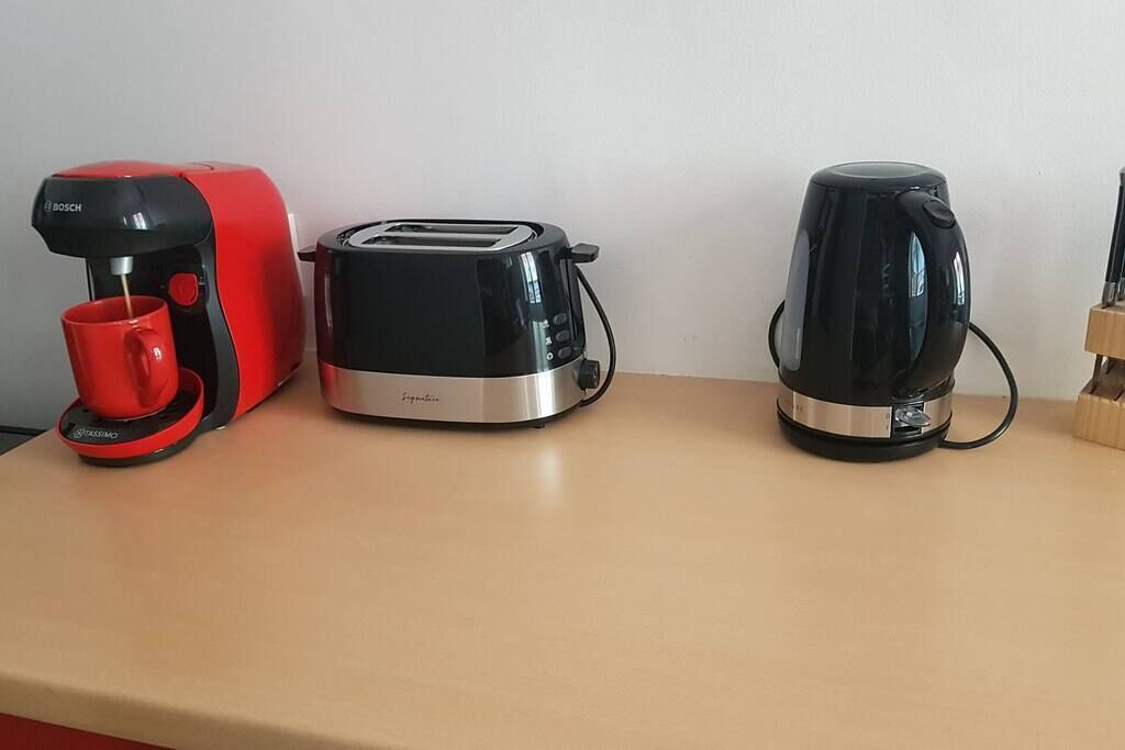 Eine Küchenarbeitsplatte mit einer roten Kaffeemaschine, einem schwarzen Toaster und einem schwarzen Wasserkocher.