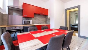 Een moderne keuken met rode kastjes, een magnetron en een eethoek met een rood-witte tafel.