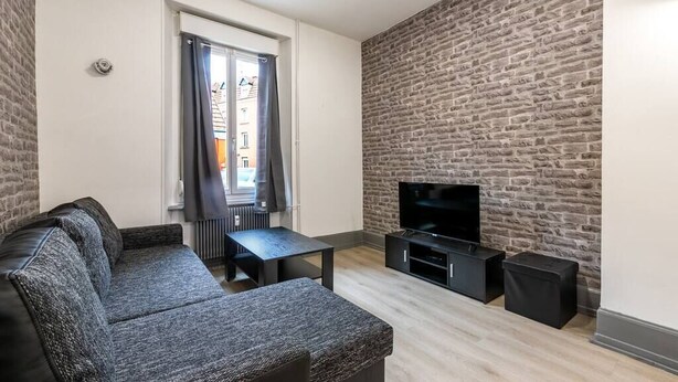 Een moderne woonkamer met een grijze bank, een zwarte salontafel, een flatscreen televisie en een muur met een stenen textuur.