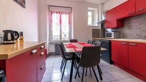 Een kleine keuken met rode kastjes, een eettafel met stoelen en een magnetron.