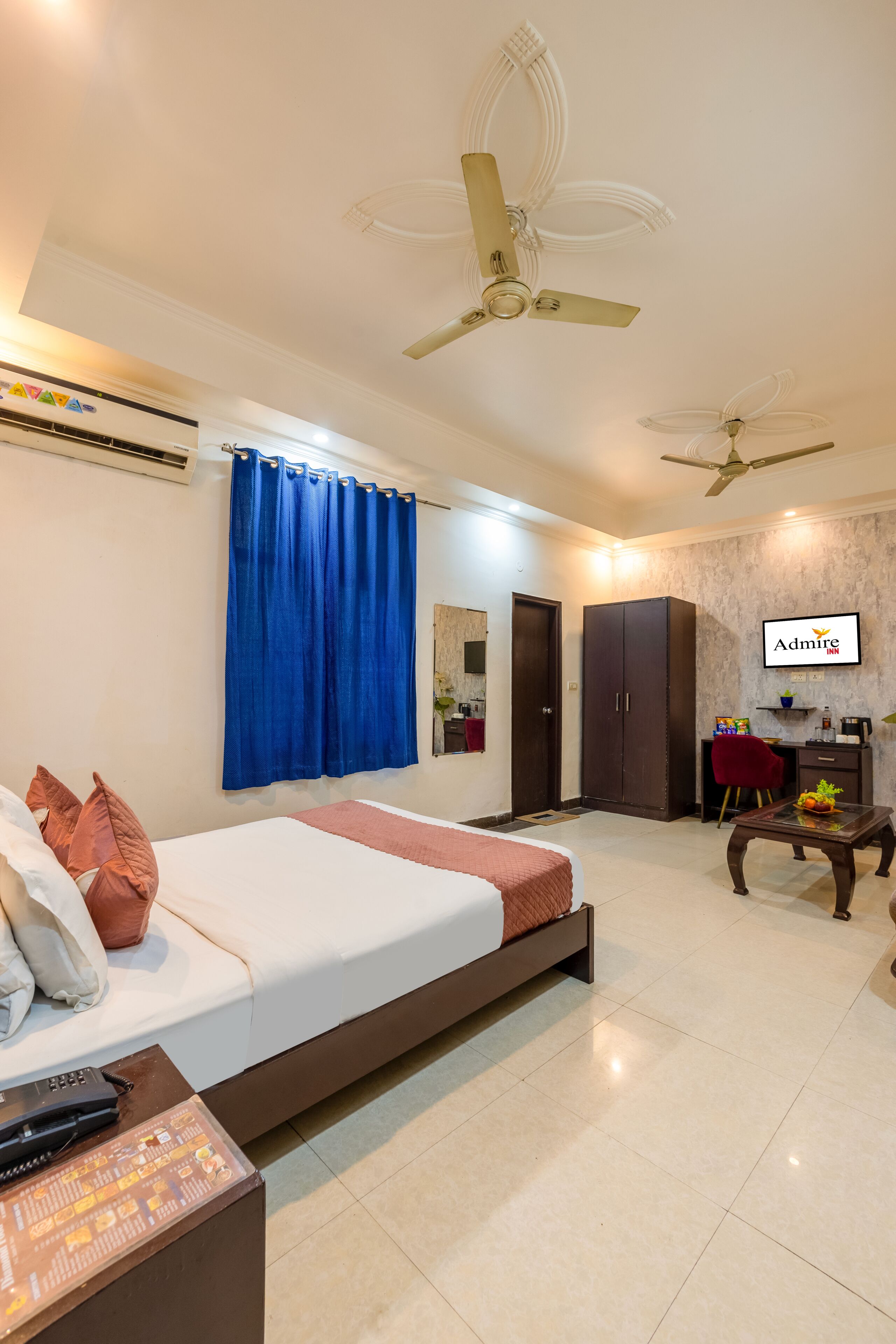 A hotel room with a bed, a desk, a TV, a wardrobe, and a ceiling fan.