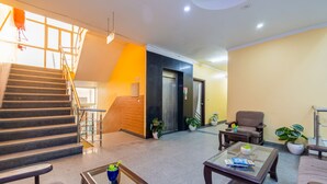A lobby with a staircase, a reception desk, seating area, and potted plants. - Hotel Diamond Stay by ASPL (Noida)