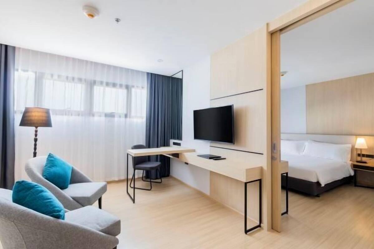 A hotel room with a bed, a desk with a TV, a chair, and a lamp.